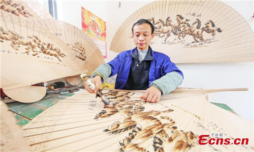 Wei Guohua shows a fan at his family workshop in Jiangxi province, Dec 24, 2016. 2,000 peasant workers from over 200 companies and family workshops in Guangchang County, Jiangxi Province, devote themselves to making pyrography fans. The fan artists have developed more than twenty types of products, including craft fan, calendar fan and folding fan, which have been sold to Japan, South Korea, Singapore, Spain and other countries, making about 100 million yuan (about $14.4 million) per year. Pyrograph is to use a hot iron to paint with iron marks.(Photo: China News Service/ Zeng Henggui)