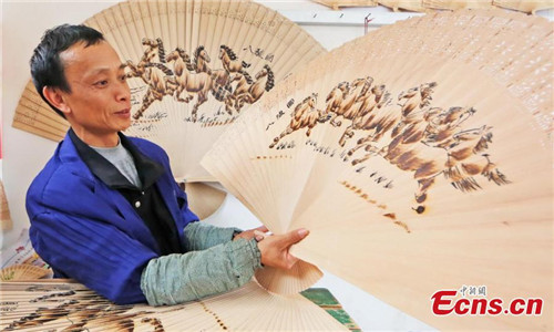 Wei Guohua shows a fan at his family workshop in Jiangxi province, Dec 24, 2016. 2,000 peasant workers from over 200 companies and family workshops in Guangchang County, Jiangxi Province, devote themselves to making pyrography fans. The fan artists have developed more than twenty types of products, including craft fan, calendar fan and folding fan, which have been sold to Japan, South Korea, Singapore, Spain and other countries, making about 100 million yuan (about $14.4 million) per year. Pyrograph is to use a hot iron to paint with iron marks.(Photo: China News Service/ Zeng Henggui)