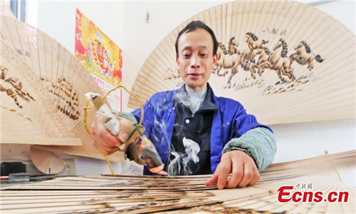 Wei Guohua shows a fan at his family workshop in Jiangxi province, Dec 24, 2016. 2,000 peasant workers from over 200 companies and family workshops in Guangchang County, Jiangxi Province, devote themselves to making pyrography fans. The fan artists have developed more than twenty types of products, including craft fan, calendar fan and folding fan, which have been sold to Japan, South Korea, Singapore, Spain and other countries, making about 100 million yuan (about $14.4 million) per year. Pyrograph is to use a hot iron to paint with iron marks.(Photo: China News Service/ Zeng Henggui)