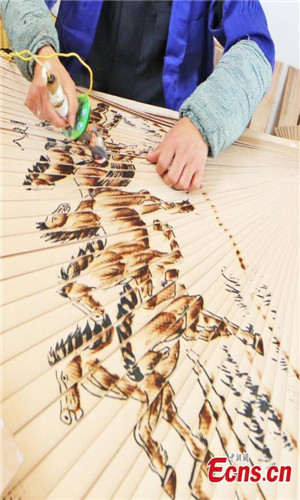 Wei Guohua shows a fan at his family workshop in Jiangxi province, Dec 24, 2016. 2,000 peasant workers from over 200 companies and family workshops in Guangchang County, Jiangxi Province, devote themselves to making pyrography fans. The fan artists have developed more than twenty types of products, including craft fan, calendar fan and folding fan, which have been sold to Japan, South Korea, Singapore, Spain and other countries, making about 100 million yuan (about $14.4 million) per year. Pyrograph is to use a hot iron to paint with iron marks.(Photo: China News Service/ Zeng Henggui)