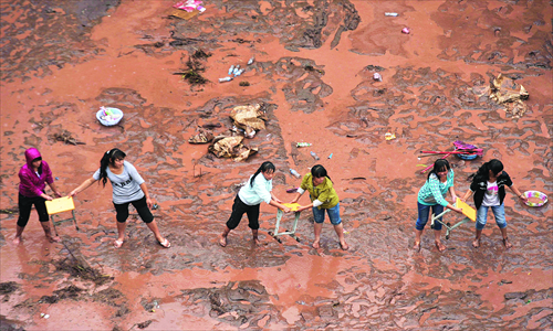 Students pass benches to drier locations after floods caused by heavy rain inundated tents that were used as temporary classrooms on Tuesday in Yiliang, Yunnan Province. Two earthquakes hit the city on Friday. Photo: CFP