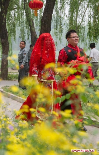 A groom and his bride walk during a group wedding held in the Old Summer Palace, or Yuanmingyuan park, in Beijing, China, May 18, 2013. A total of 30 couples of newlyweds took part in event with traditional Chinese style here on Saturday. (Xinhua/Luo Xiaoguang)  