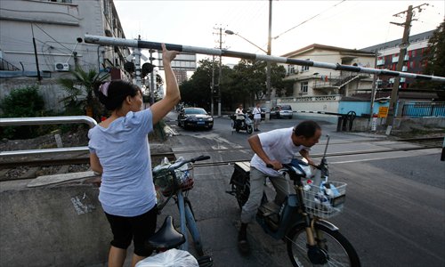 Bike riders help each other sneak under the security gates at the crossing on Songhuajiang Road even though a train is due. Photo: Yang Hui/GT