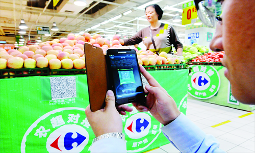 A consumer scans the quick response (QR) code for apples in a Carrefour supermarket in Luoyang, Central China's Henan Province Wednesday. QR codes are available for agricultural products such as apples, pears, and green beans sold at many of the chain's supermarkets nationwide. Consumers can scan the codes to get information about the products, including places of origin as well as names and certificates of planters. Photo: CFP