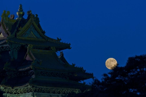 A full moon sets behind a building of the Forbidden City in Beijing, capital of China, June 23, 2013. The moon looks 14 percent larger and 30 percent brighter than usual on Sunday. The scientific term for the phenomenon is 