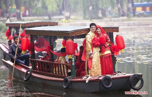 A couple of newlyweds board on a boat during a group wedding held in the Old Summer Palace, or Yuanmingyuan park, in Beijing, China, May 18, 2013. A total of 30 couples of newlyweds took part in event with traditional Chinese style here on Saturday. (Xinhua/Zhao Bing)  