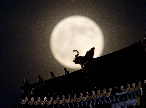 A full moon sets behind a building of the Forbidden City in Beijing, capital of China, June 23, 2013. The moon looks 14 percent larger and 30 percent brighter than usual on Sunday. The scientific term for the phenomenon is 