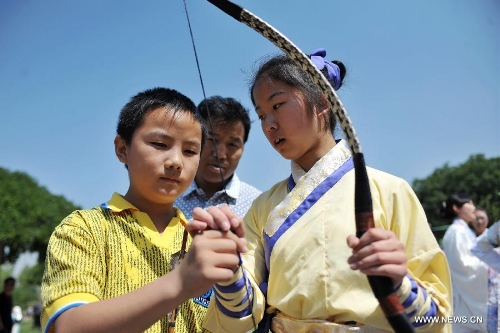 Wang Yawen (R), who is fond of the Han Chinese culture, introduces traditional archery to a boy during a celebration activity of the Dragon Boat Festival, in Lanzhou, capital of northwest China's Gansu Province, June 12, 2013. Wednesday marks the Dragon Boat Festival, a festival which falls on May 5 each year in lunar calendar in China. Local residents in Lanzhou held a series of celebration activities by the riverside of the Yellow River on this day. (Xinhua/Chen Bin) 