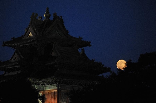 A full moon sets behind a building of the Forbidden City in Beijing, capital of China, June 23, 2013. The moon looks 14 percent larger and 30 percent brighter than usual on Sunday. The scientific term for the phenomenon is 