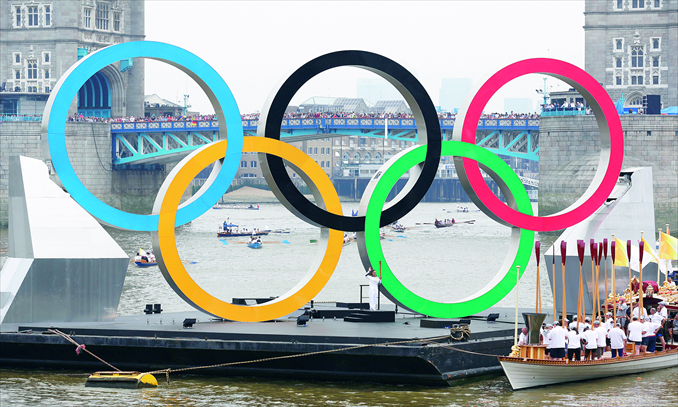 Locals watch as giant Olympic rings mounted on a barge float on the River Thames in front of Tower Bridge during the 2012 London Olympic Games Torch Relay on Friday. Photo:  AFP