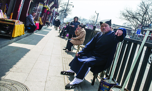 A feng shui master waits for customers on Yonghegong Dajie. Some of them burn offerings in metal buckets along the street.  Photo: Li Hao/GT