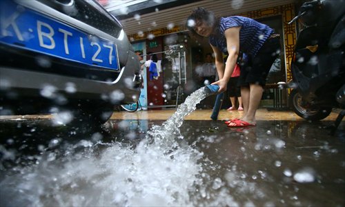 In Putuo district, on Lishan Road, a shop owner uses a pump to drain the rainwater that flooded her shop. Photo: Cai Xianmin/GT