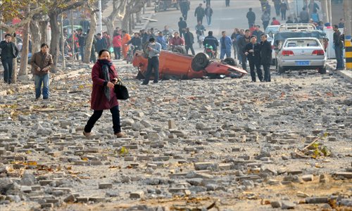 A woman walks through a rubble-strewn street on Friday in Huangdao district, Qingdao in East China's Shandong Province after explosions caused by a leaky pipeline ripped roads apart and turned cars over. Photo: IC