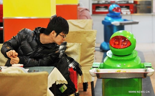 A customer watches a robot serving dishes in a robot themed restaurant in Harbin, capital of northeast China's Heilongjiang Province, Jan. 18, 2013. Opened in June of 2012, the restaurant has gained fame by using a total of 20 robots to cook meals, deliver dishes and greet customers. (Xinhua/Wang Jianwei) 