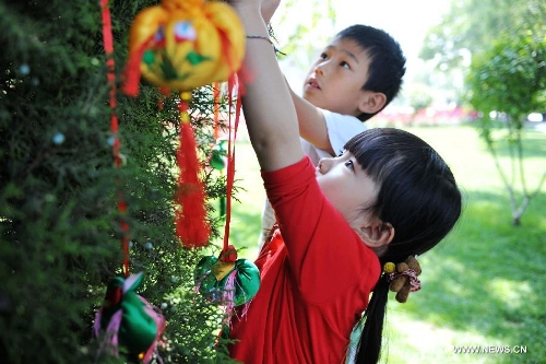 Children hang perfume pouches for blessings onto a tree during a celebration activity of the Dragon Boat Festival, in Lanzhou, capital of northwest China's Gansu Province, June 12, 2013. Wednesday marks the Dragon Boat Festival, a festival which falls on May 5 each year in lunar calendar in China. Local residents in Lanzhou held a series of celebration activities by the riverside of the Yellow River on this day. (Xinhua/Chen Bin) 