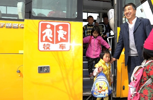 Safety staff Rui Qihua helps pupils to get off a school bus in Zhongwei City, northwest China's Ningxia Hui Autonomous Region, March 29, 2013. (Xinhua/Li Ran)