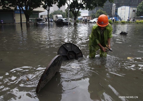 A sanitation worker opens manhole covers on a flooded road in Jinjiang City, southeast China's Fujian Province, May 16, 2013. A torrential rainfall hit the city overnight, flooding many roads in the city. (Xinhua)  