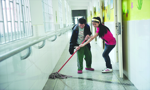 Qiu Jian teaches a handicapped boy to mop the floor. Photo: CFP