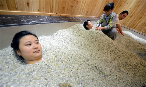 Two customers are buried under sand to relax and experience sand therapy in Nanjing, Jiangsu Province on Wednesday. The sand is made from jade and magnets from the Xinjiang Uyghur Autonomous Region, where it has been used to treat arthritis and similar health conditions. The treatment has recently become popular in the city. Photo: CFP