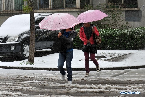 Citizens holding umbrellas walk on a snowy road in Taiyuan, capital of north China's Shanxi Province, April 19, 2013. A cold front brought snowfall to the city on April 19 morning. (Xinhua/Zhan Yan)