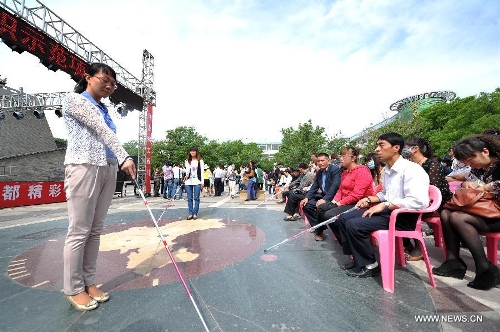 A worker introduces to the blind people the way of using a crutch by voice at the Yuhuangge Square in Yinchuan City, capital of northwest China's Ningxia Hui Autonomous Region, May 14, 2013. An activity aimed at helping the blind to walk was held here on Tuesday, in which more than 100 blind people were provided with crutches as they were helped to walk with them ahead of the 23rd national day for helping the disabled on May 19. (Xinhua/Peng Zhaozhi) 