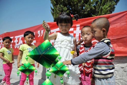 Wang Haorong (C) and several other children play a sachet during a celebration activity of the Dragon Boat Festival, in Lanzhou, capital of northwest China's Gansu Province, June 12, 2013. Wednesday marks the Dragon Boat Festival, a festival which falls on May 5 each year in lunar calendar in China. Local residents in Lanzhou held a series of celebration activities by the riverside of the Yellow River on this day. (Xinhua/Chen Bin) 