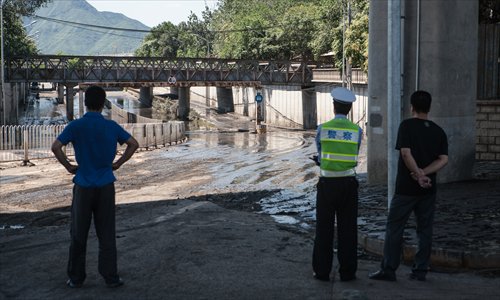 A policeman and two residents look at the water and mud that blocked the traffic at Mayu Bridge in Mentougou district during the July 21 rainstorm. Photo: Li Hao/GT