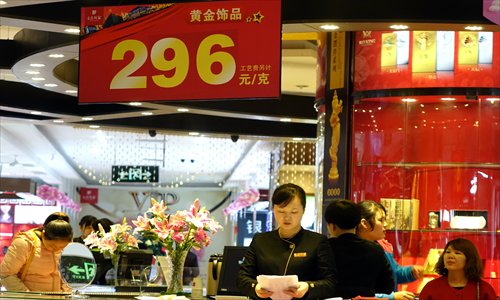 A salesperson stands under a sign showing the price of gold, at 296 yuan ($48.76) per gram in Zhengzhou, Central China's Henan Province on Tuesday. Since the beginning of this year, the international gold price has fallen more than 25 percent. The price of gold closed at $1,253.17 an ounce on Tuesday in Hong Kong. Photo:CFP