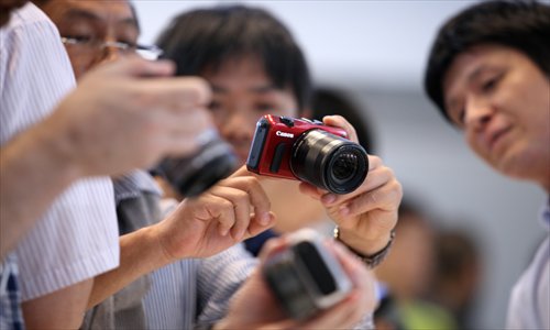 Members of the media try Canon EOS M mirrorless interchangeable-lens cameras at its unveiling in Tokyo, Japan, on Monday. Canon Inc, the world's biggest camera maker, will start selling its first mirrorless model in September as demand shifts away from traditional point-and-shoot cameras. Photo: CFP
