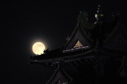 A full moon sets behind a building of the Forbidden City in Beijing, capital of China, June 23, 2013. The moon looks 14 percent larger and 30 percent brighter than usual on Sunday. The scientific term for the phenomenon is 