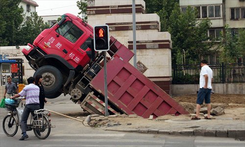 A truck is trapped in a ditch after falling through the metal plate  covering it, near a residential community in Changping district Wednesday. The truck was removed overnight, and the road repaired yesterday morning. Photo: CFP