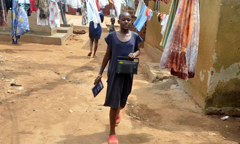 A girl carrying a radio walks in a neighborhood in Kampala, Uganda, June 14, 2021. (Photo: Xinhua)