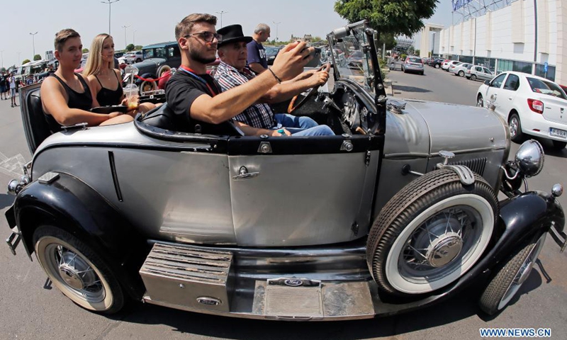 People pose for photos in a vintage car during the Old Cars Show 2021 organized by Romania's Vintage Vehicle Club in Bucharest, Romania, July 31, 2021.(Photo: Xinhua)