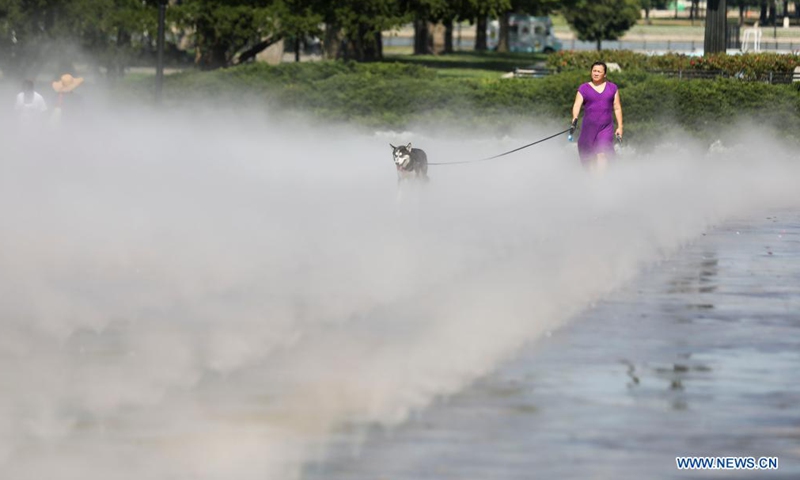 A woman walks her dog in the mist garden near the Unisphere in Flushing Meadows Corona Park in New York, the United States, Aug. 13, 2021. A heat wave recently hit New York City.Photo:Xinhua