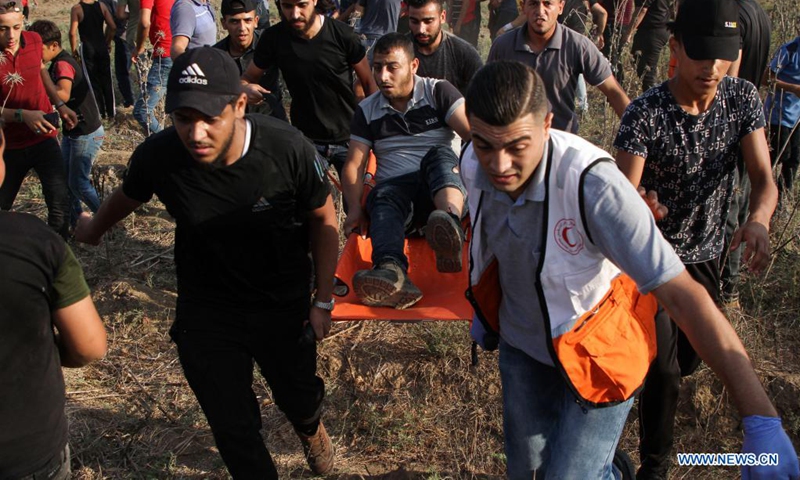 People carry an injured man during a protest to mark 52nd anniversary of burning Al-Aqsa Mosque in East Jerusalem, on the Gaza-Israel border in east of southern Gaza Strip city of Khan Younis, Aug. 21, 2021. Dozens of Palestinian protesters were injured on Saturday in clashes with Israeli soldiers near the border between eastern Gaza Strip and Israel, Palestinian medics said. (Photo: Xinhua)