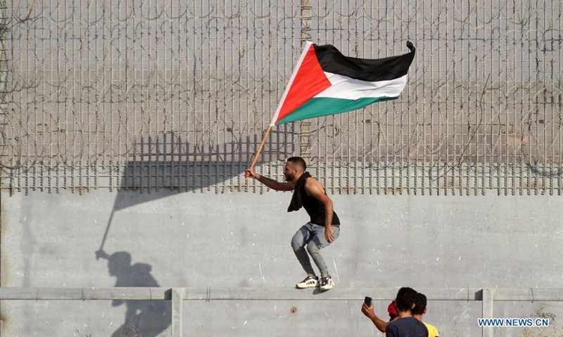 A protester holds a Palestinian flag during a protest to mark 52nd anniversary of burning Al-Aqsa Mosque in East Jerusalem, on the Gaza-Israel border in east of southern Gaza Strip city of Khan Younis, Aug. 21, 2021. Dozens of Palestinian protesters were injured on Saturday in clashes with Israeli soldiers near the border between eastern Gaza Strip and Israel, Palestinian medics said.(Photo: Xinhua)