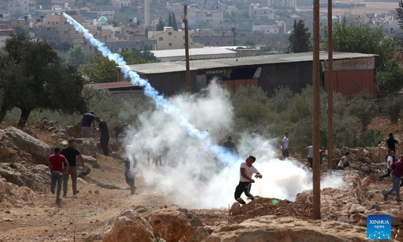 A Palestinian protester uses a slingshot to throw back a tear gas canister fired by Israeli soldiers during a protest against the expansion of Jewish settlements in the West Bank village of Beit Dajan, east of Nablus, Oct. 15, 2021.Photo:Xinhua