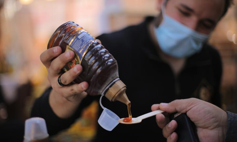 A vendor pours a spoon of honey to a visitor for tasting during the 3rd Egyptian Honey Festival in Giza, Egypt, Nov. 24, 2021.(Photo: Xinhua)