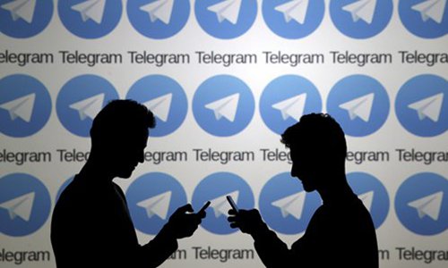 Two men pose with smartphones in front of a screen showing the Telegram logos. Photo: VCG