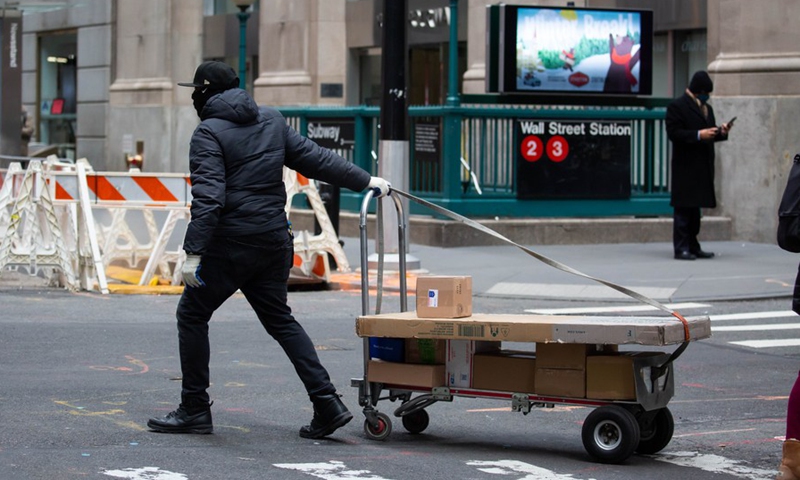 A delivery worker rolls packages across Wall Street in New York, United States, Jan. 8, 2021. (Photo by Michael Nagle/Xinhua)