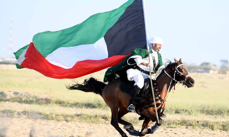 A man carrying a Kuwaiti national flag rides a horse during an equestrian show in Mubarak Al-Kabeer Governorate, Kuwait, Feb. 25, 2021. (Photo by Ghazy Qaffaf/Xinhua)