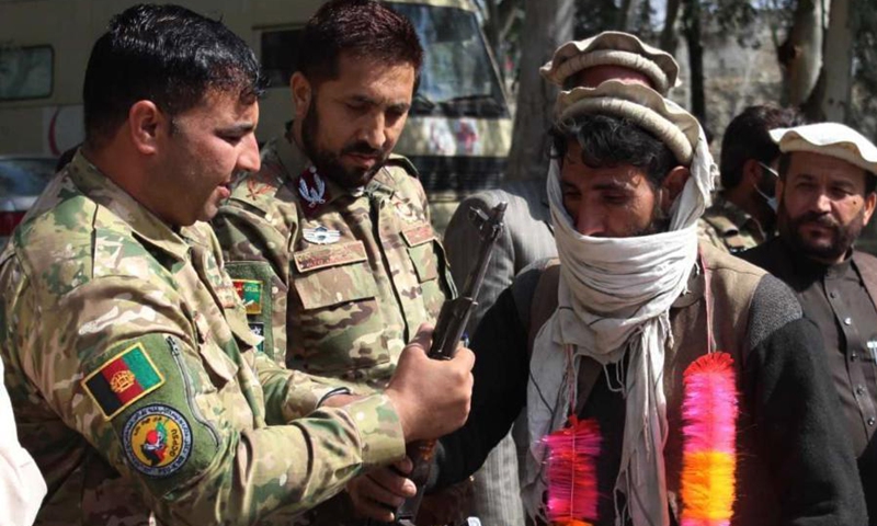 A militant (R front) hands over a weapon to a local official during a surrender ceremony in Asadabad, capital of Kunar province, Afghanistan, March 10, 2021. Twenty-five militants on Wednesday surrendered to the government authorities in Afghanistan's eastern Kunar province, the province governor said.(Photo: Xinhua)