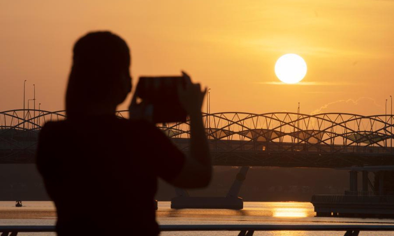 A woman takes photos of the sunrise at the Merlion Park in Singapore, on March 16, 2021.(Photo: Xinhua)