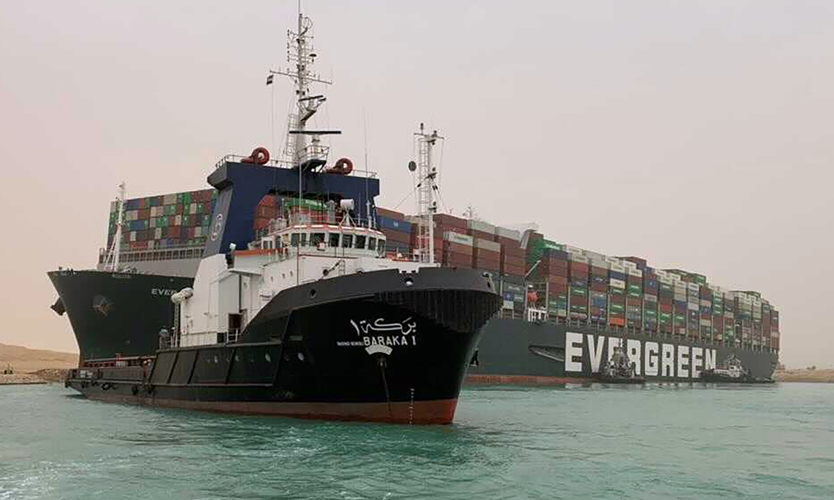 A tug navigates near ultra-large container ship the Ever Given which is operated by Evergreen Marine Corp based in the island of Taiwan,with its bow stuck into the bank of the Suez Canal in Egypt on Wednesday. The vessel turned sideways amid stormy weather, blocking traffic in the crucial East-West waterway for global shipping. An Egyptian official warned on Wednesday it could take at least two days to move the ship.  Photo: VCG