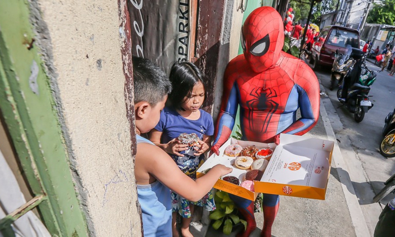 A man dressed as Spider-Man distributes donuts to children affected by the COVID-19 lockdown outside their home in Manila, the Philippines on April 27, 2021.Photo:Xinhua