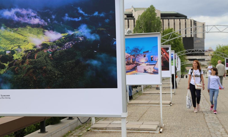 People walk past display panels of a photo exhibition entitled Cases of Poverty Alleviation through Tourism in China in Sofia, Bulgaria, on May 5, 2021. The photo exhibition entitled Cases of Poverty Alleviation through Tourism in China opened here on Wednesday.(Photo: Xinhua)