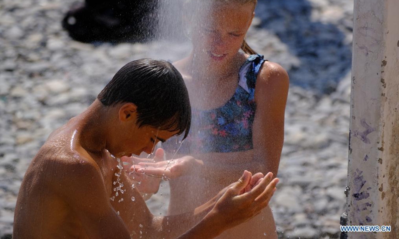 Children take showers on a beach during hot weather in Nice, France, Aug. 14, 2021. (Photo by Serge Haouzi/Xinhua)