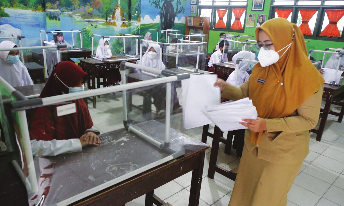 A teacher (right) gives papers to students attending a class using safety separators during the first day back to school programs in Bandar Lampung, Indonesia on Monday. Photo: AFP