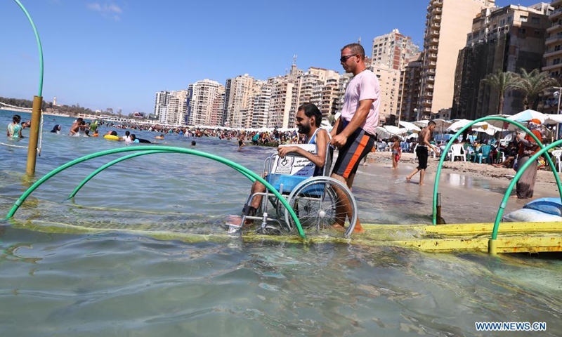 A beach worker helps a wheelchaired man reach the sea on a disability-friendly public beach in Alexandria, Egypt, on Aug. 17, 2021.(Photo: Xinhua)