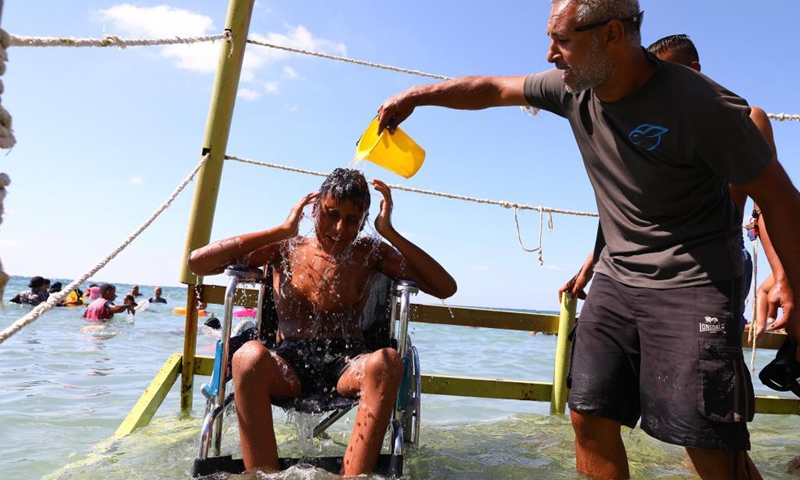 A beach worker helps a wheelchaired boy enjoy himself on a disability-friendly public beach in Alexandria, Egypt, on Aug. 17, 2021.(Photo: Xinhua)